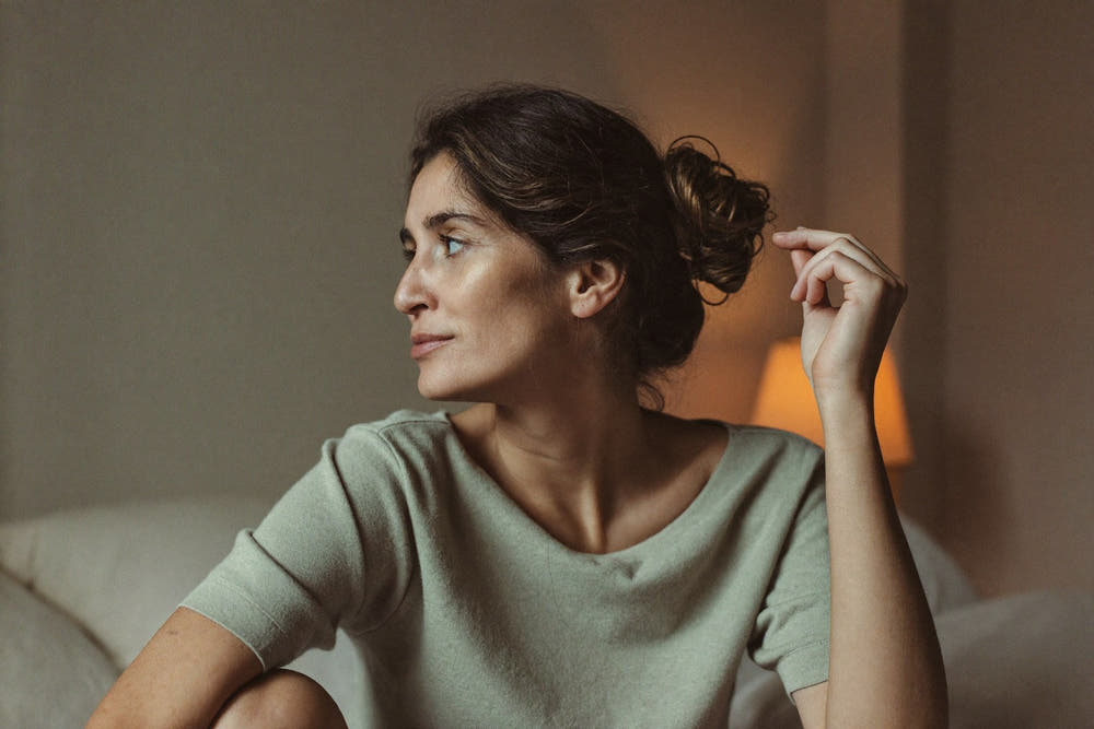 A woman in a soft knit top touching her parting in warm evening lamplight