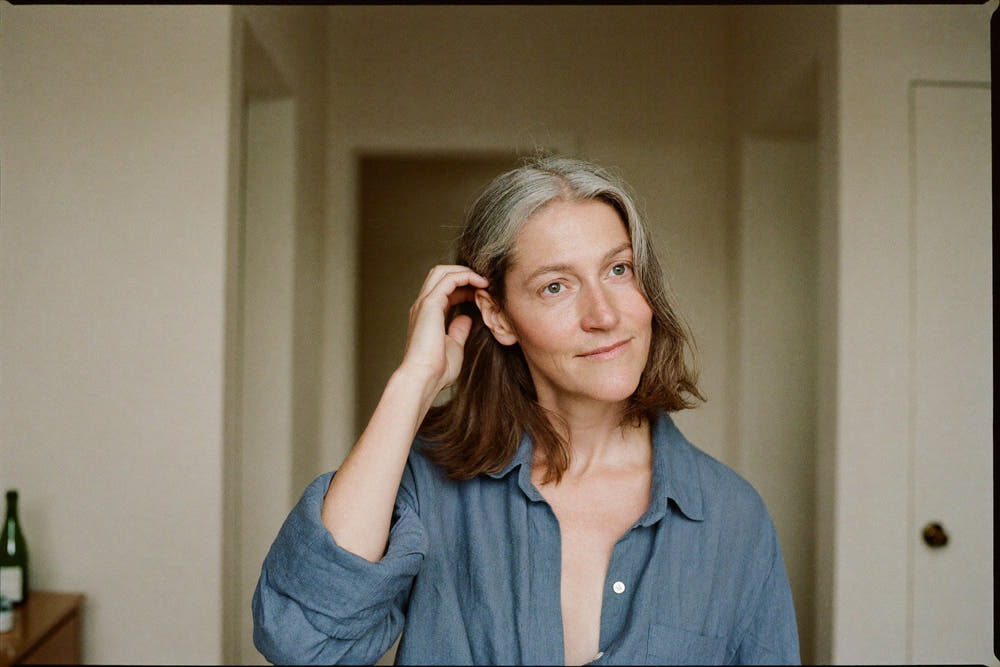 A woman in her early fifties with greying shoulder-length hair running her fingers through it