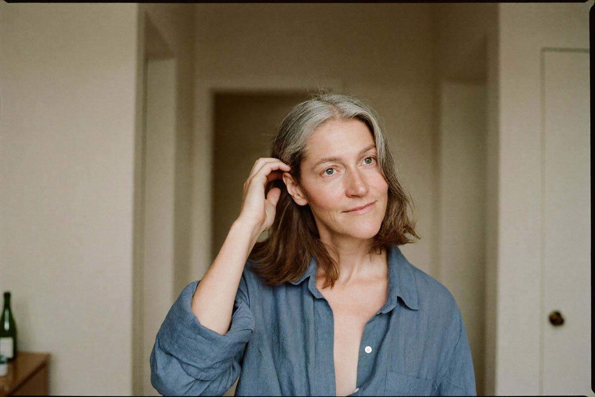 A woman in her early fifties with greying shoulder-length hair running her fingers through it