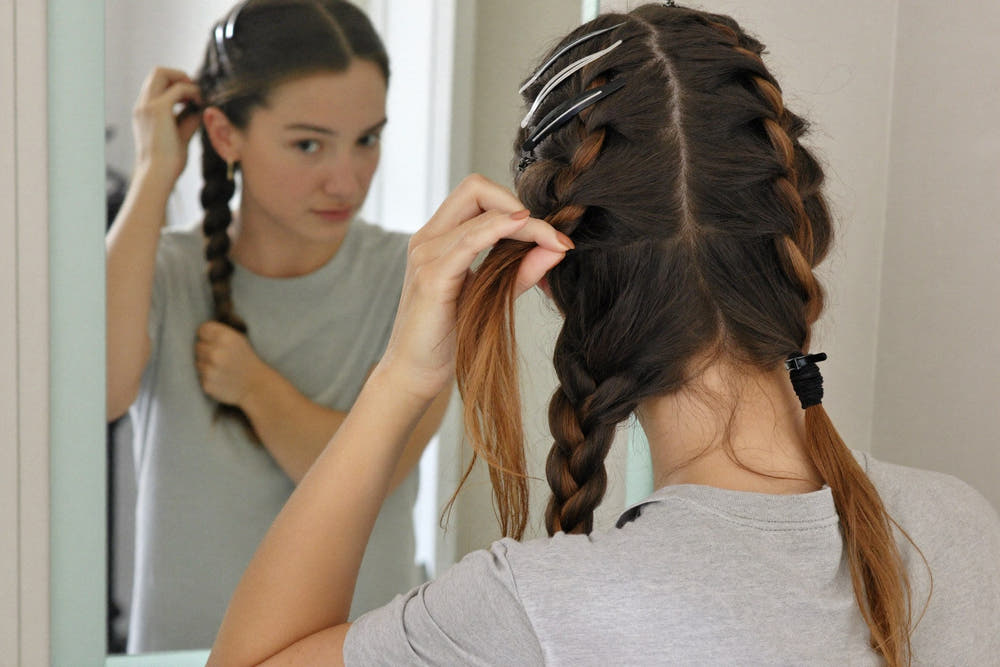 A woman in a soft grey t-shirt sectioning dry hair with clips at a bright mirror