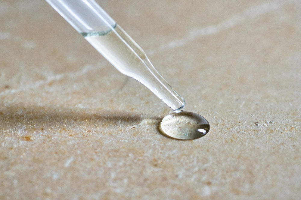 A glass pipette releasing a single clear drop onto a pale stone surface