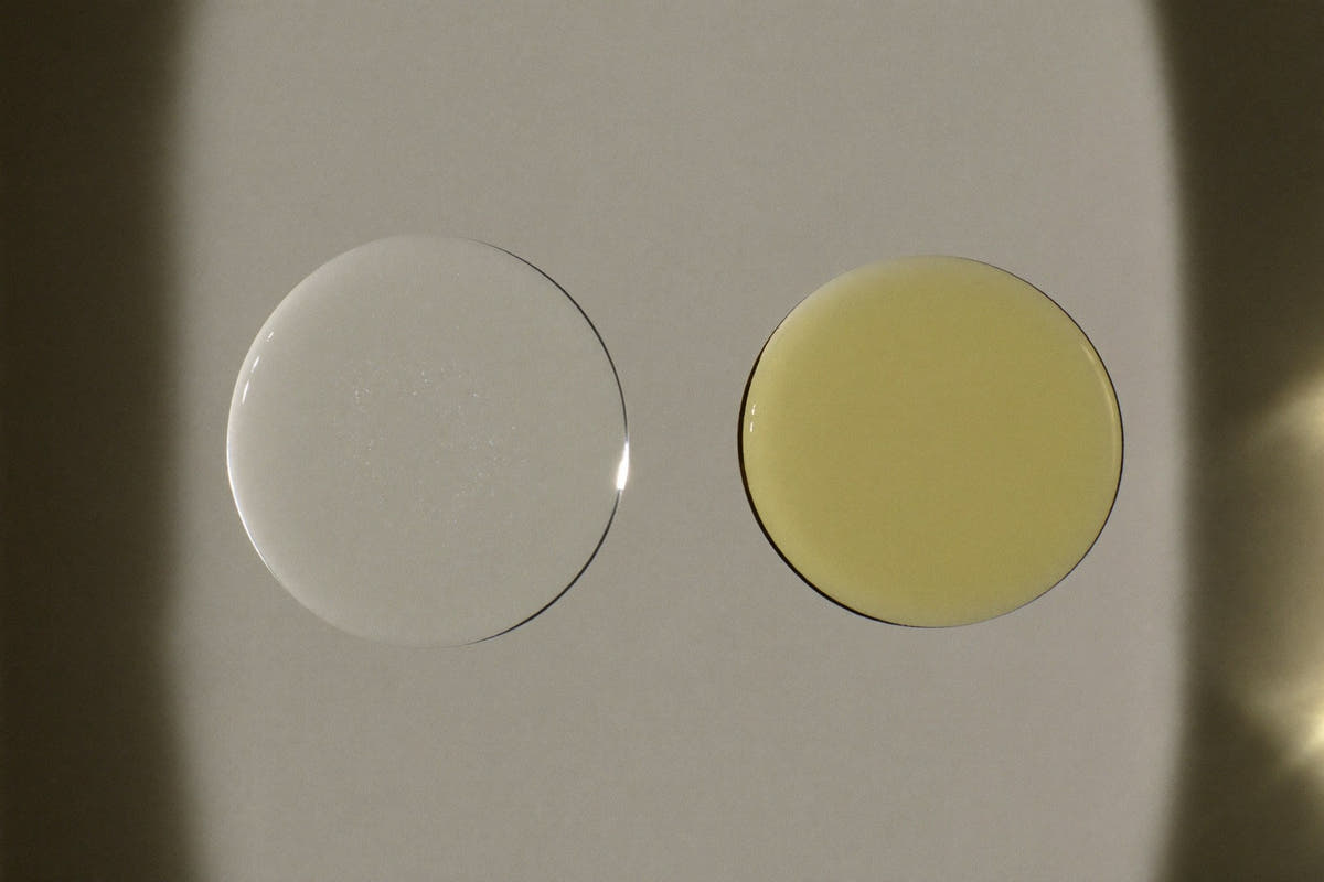 Two drops on a pane of glass, lit from the side: one a clear round bead, one a golden oil drop spreading thin