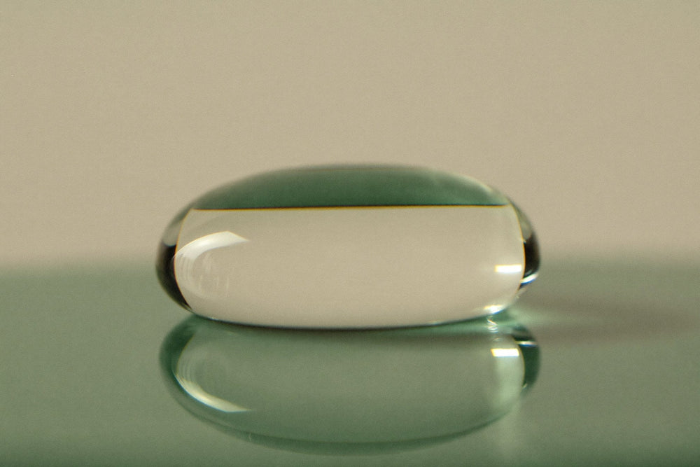 A single clear drop of liquid resting on a pane of glass, lit from the side