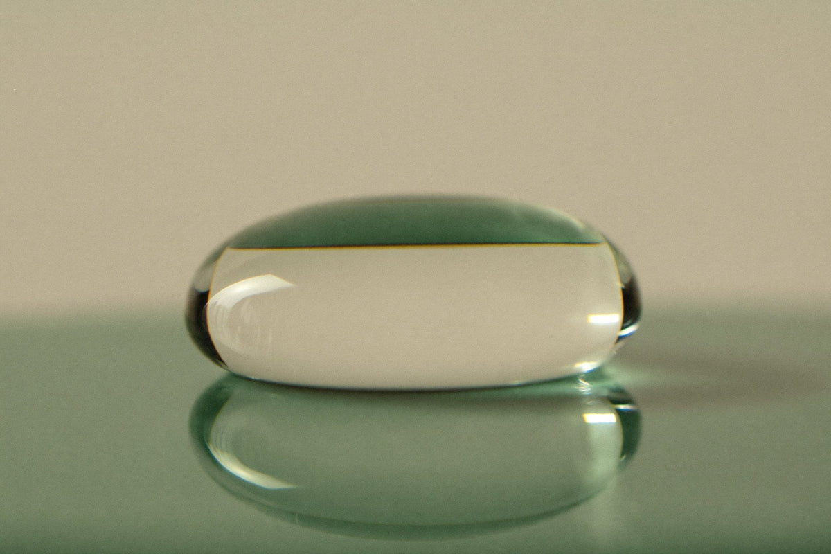 A single clear drop of liquid resting on a pane of glass, lit from the side