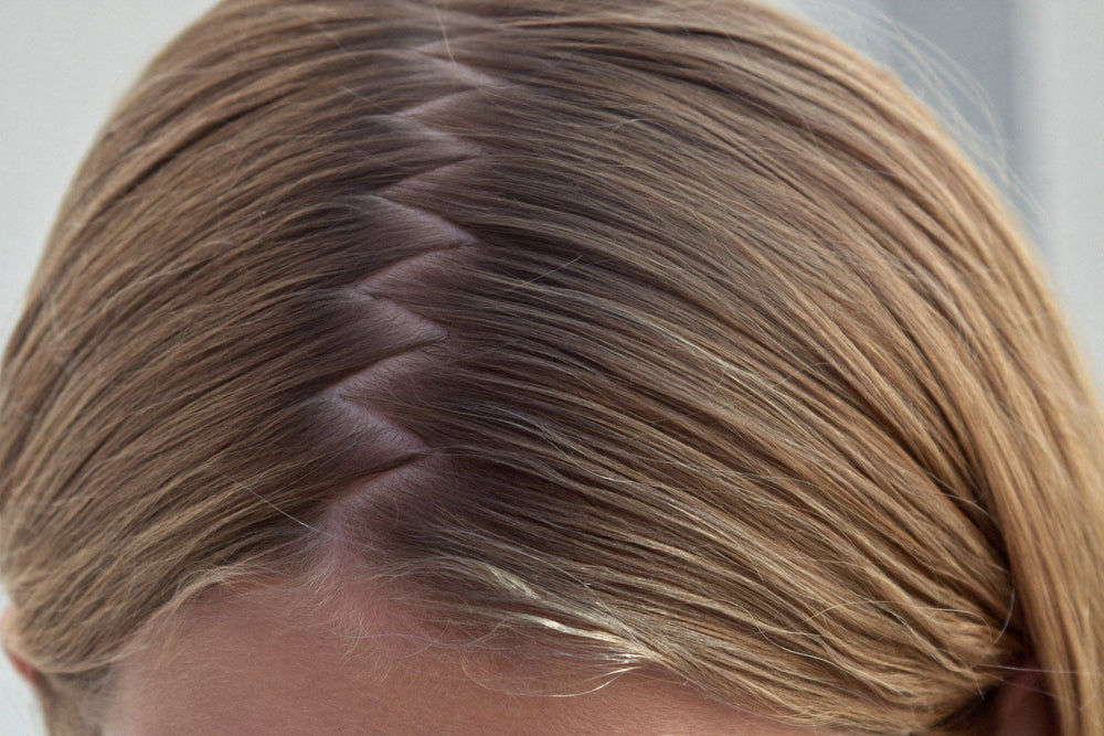 Close view of a zigzag part in light brown hair, made with the tail of a comb