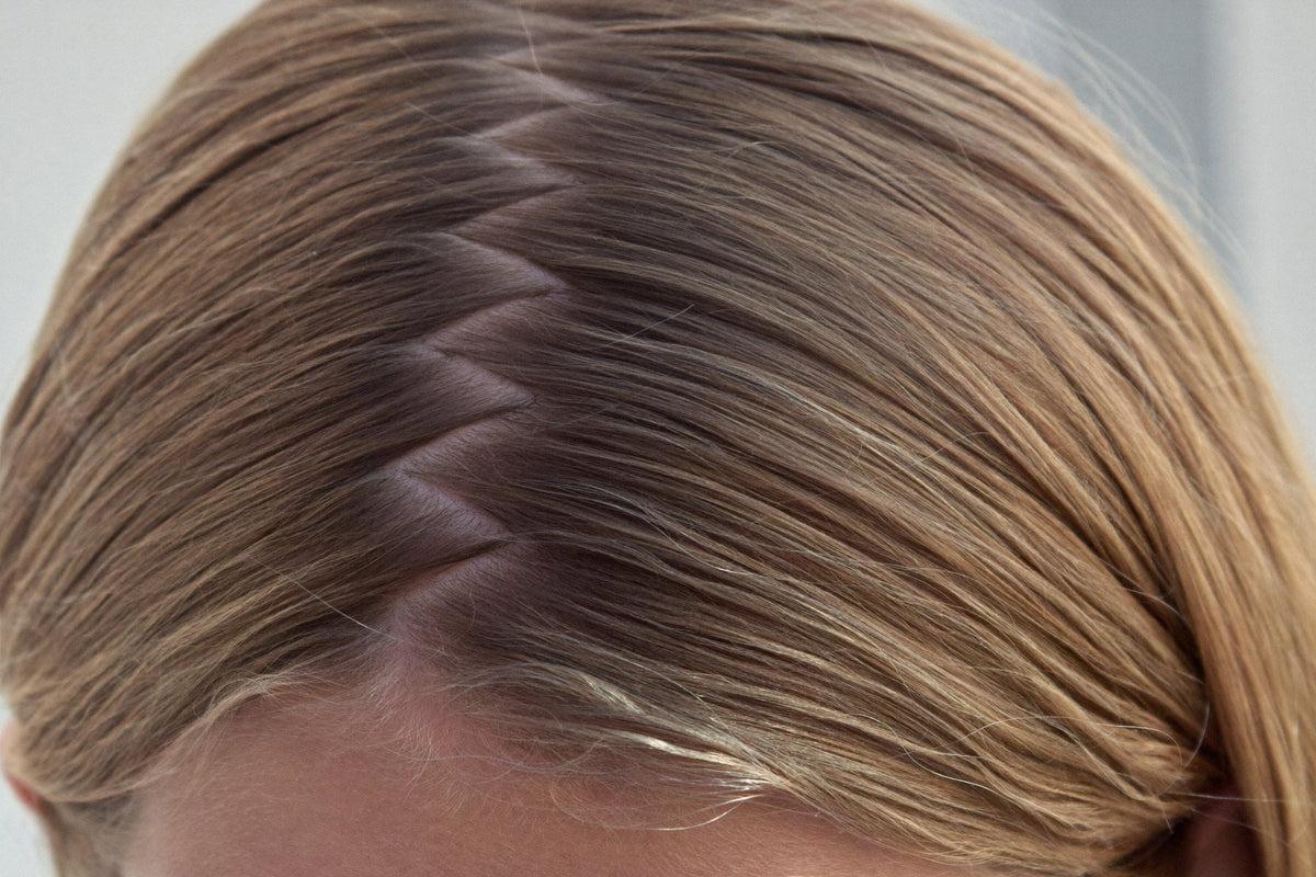 Close view of a zigzag part in light brown hair, made with the tail of a comb