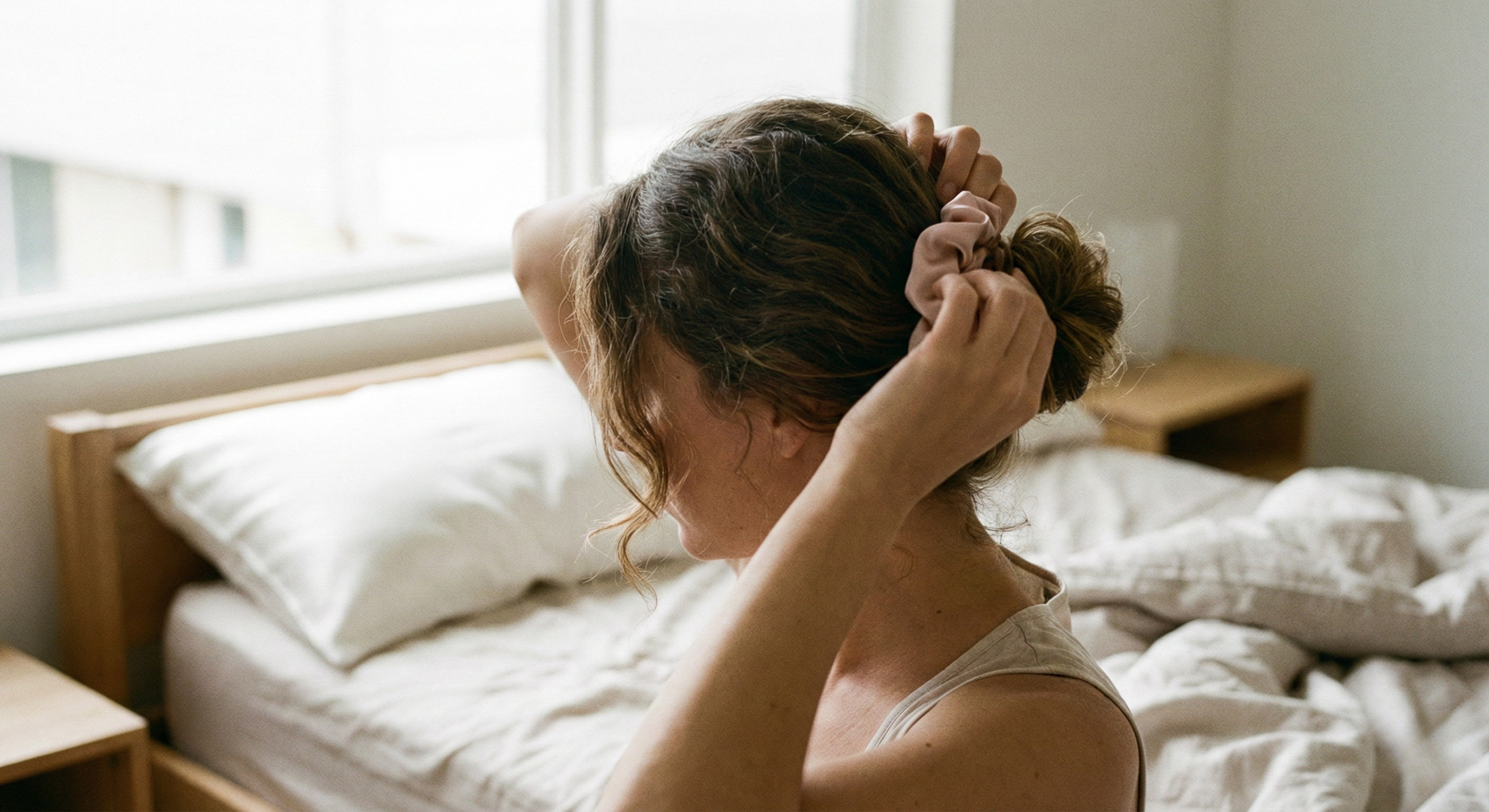 Woman using satin scrunchie and silk pillowcase habits to reduce breakage and protect regrowth